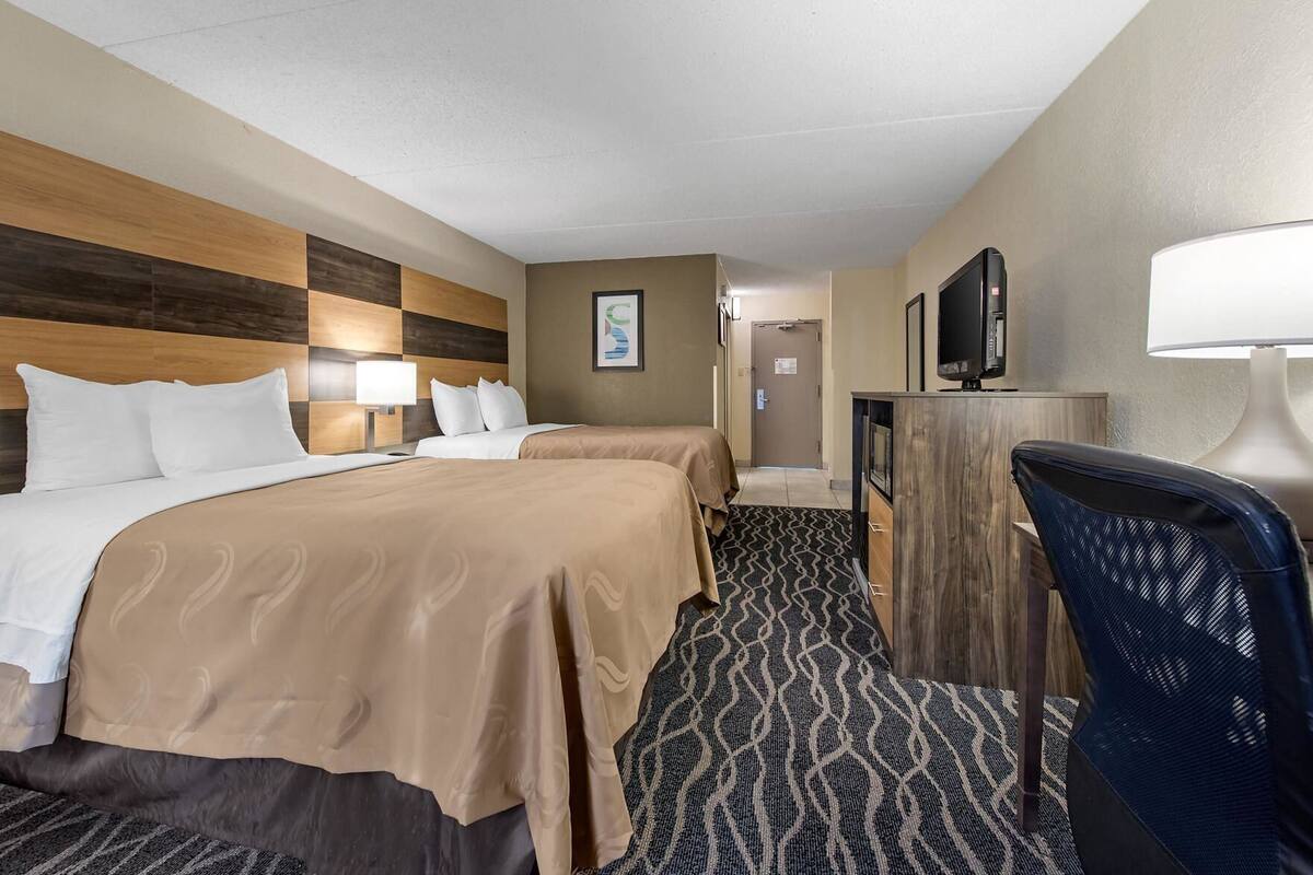 A hotel room with two beds, a desk, a chair, a TV, and a framed picture on the wall.