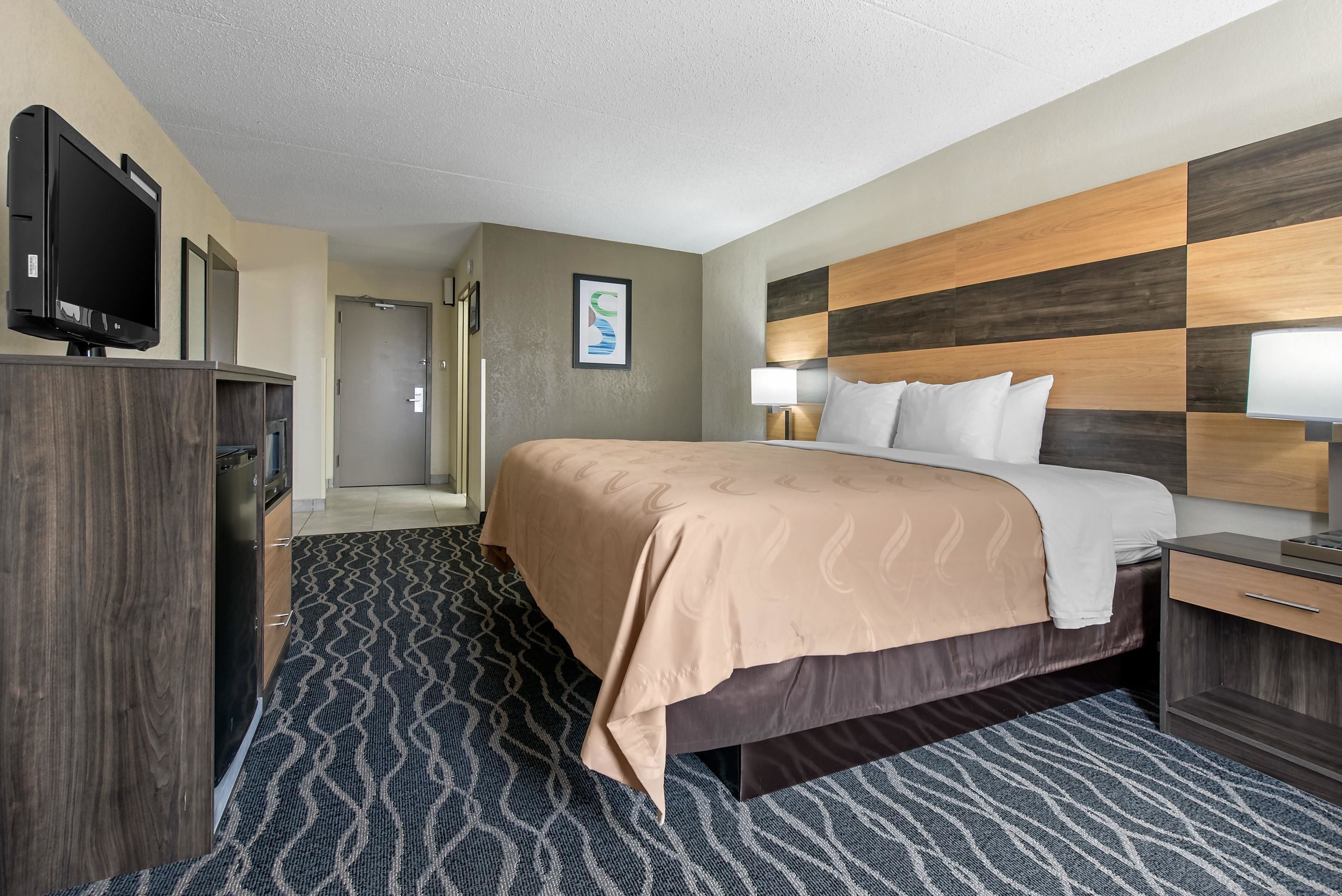 A hotel room with a bed, a TV, a desk, and a bathroom door.