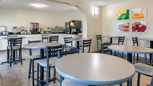 Un café avec des tables et des chaises rondes, une machine à café et un réfrigérateur.