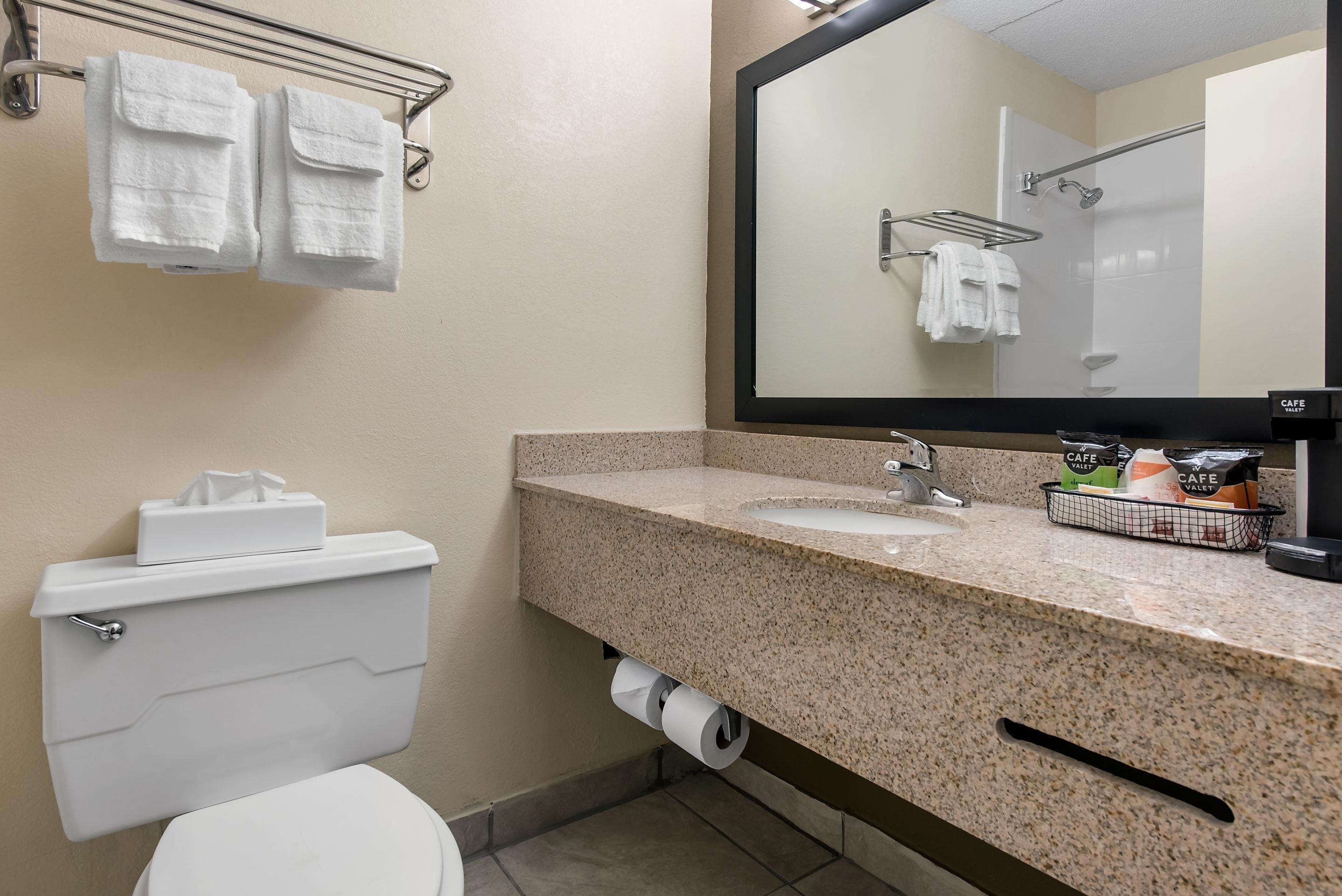 A bathroom with a toilet, sink, and mirror. There are towels hanging on a rack and a basket of toiletries on the sink.
