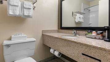 A bathroom with a toilet, sink, and mirror. There are towels hanging on a rack and a basket of toiletries on the sink.