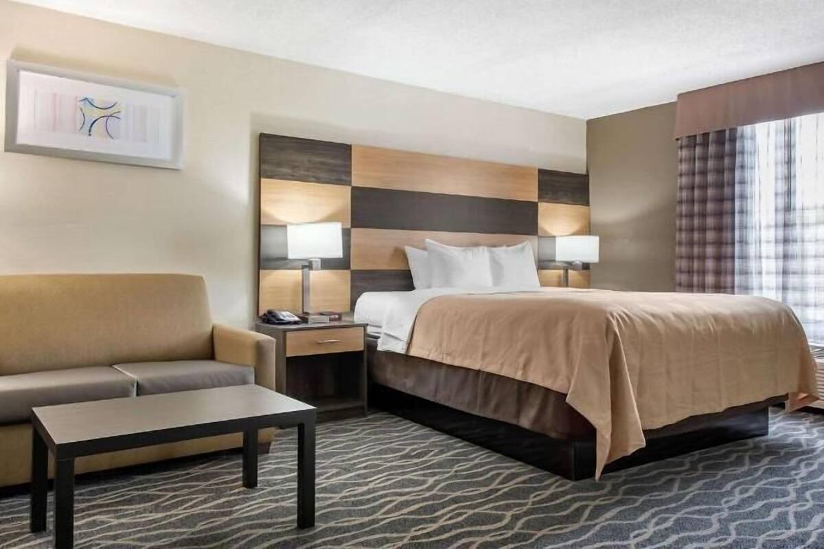 A hotel room with a bed, a sofa, a coffee table, a nightstand, and a lamp.