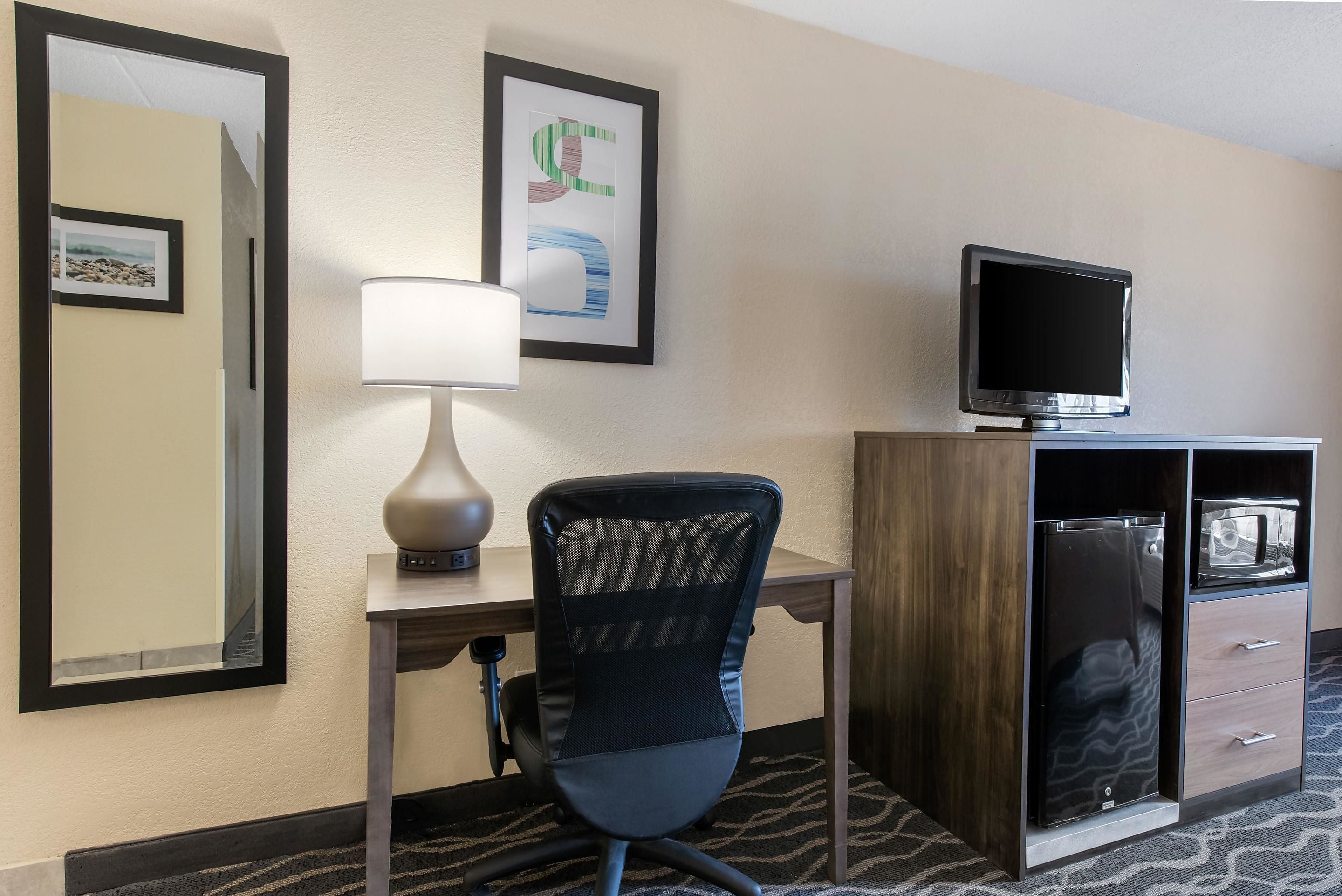 A hotel room with a desk, chair, TV, and a minibar.