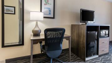 A hotel room with a desk, chair, TV, and a minibar.