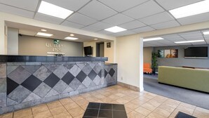 Un espace d’accueil d’hôtel comprenant un comptoir de réception, un téléviseur à écran plat, un canapé vert et un sol carrelé.