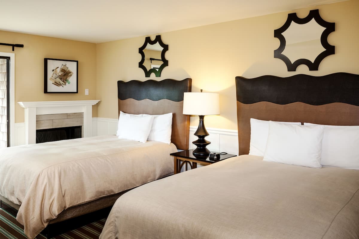 A hotel room with two beds, a fireplace, and decorative mirrors on the walls.