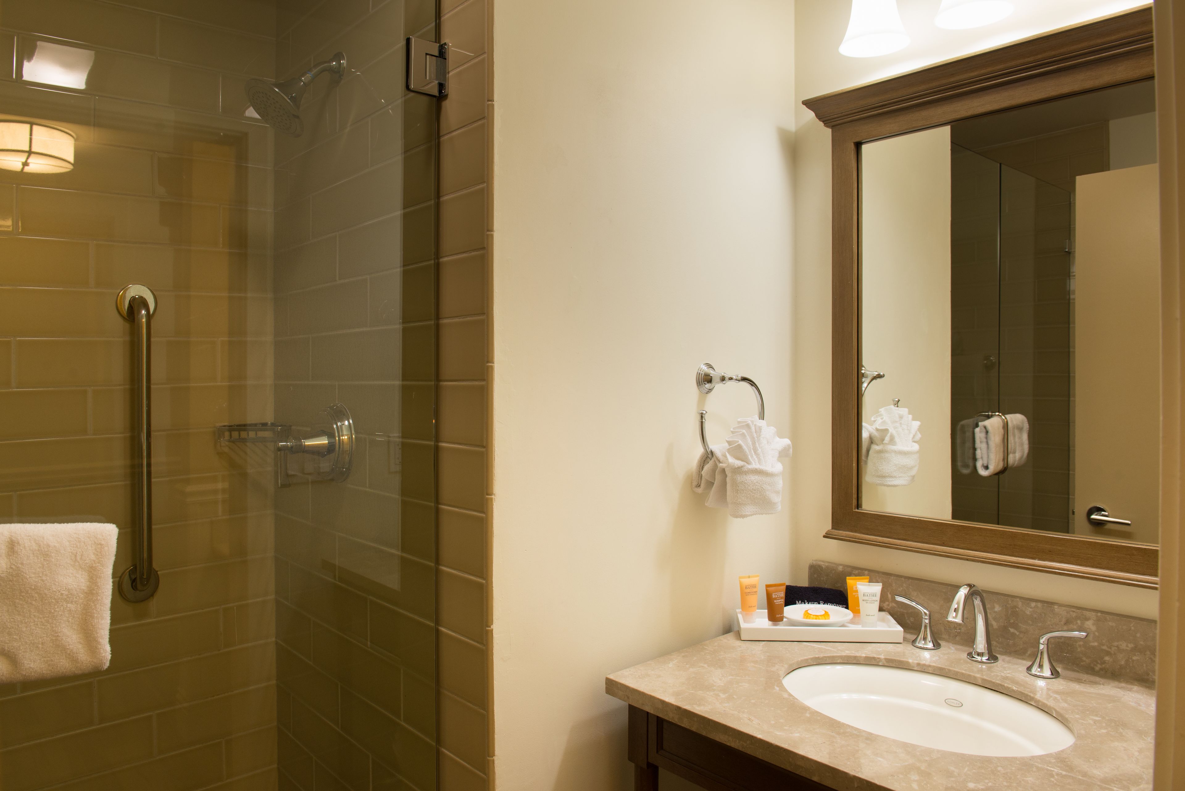A bathroom with a glass shower enclosure, a sink with two faucets, and a mirror above the sink.