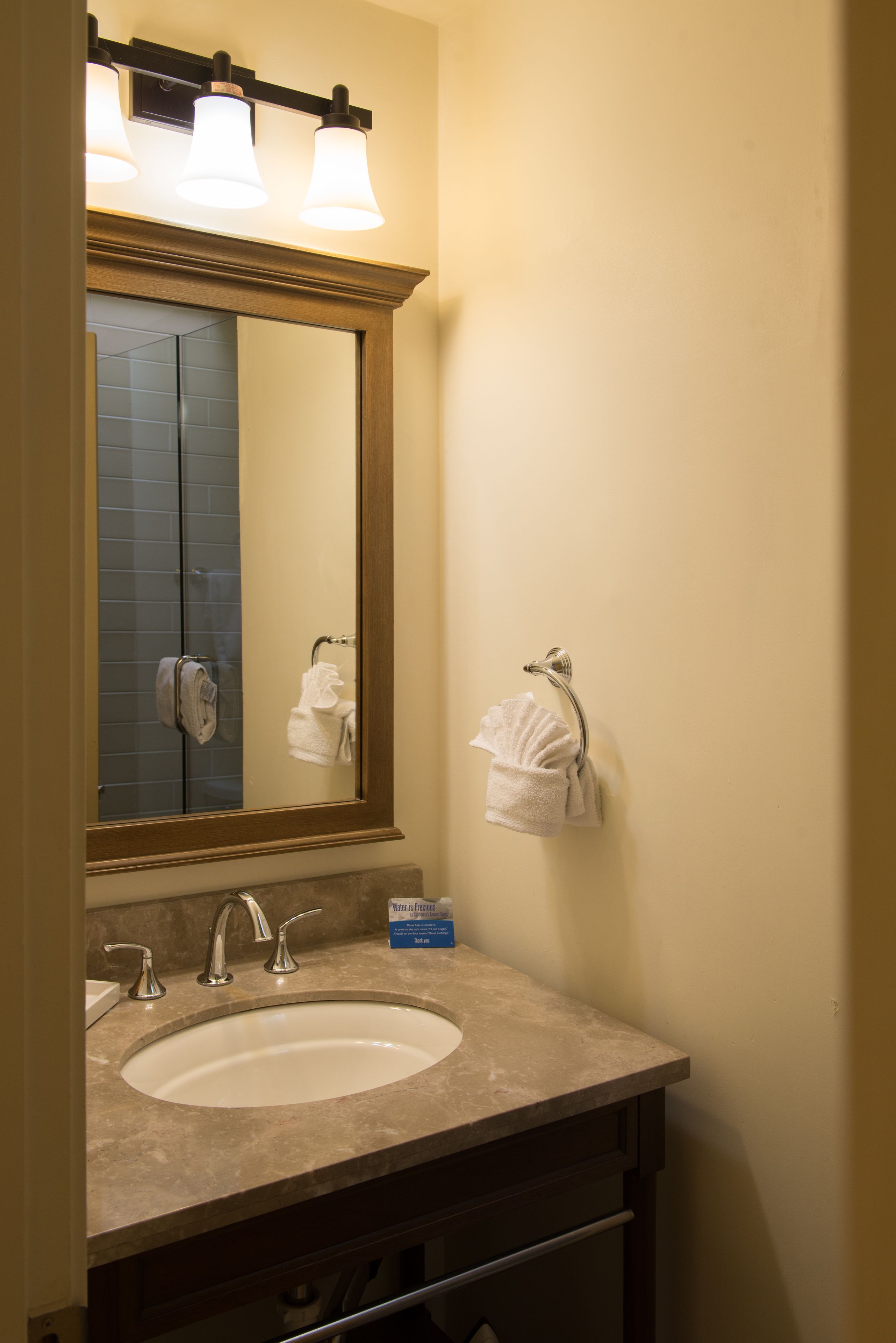 Une salle de bain équipée d’un lavabo, d’un miroir, d’un porte-serviettes et d’une boîte contenant des articles de toilette.