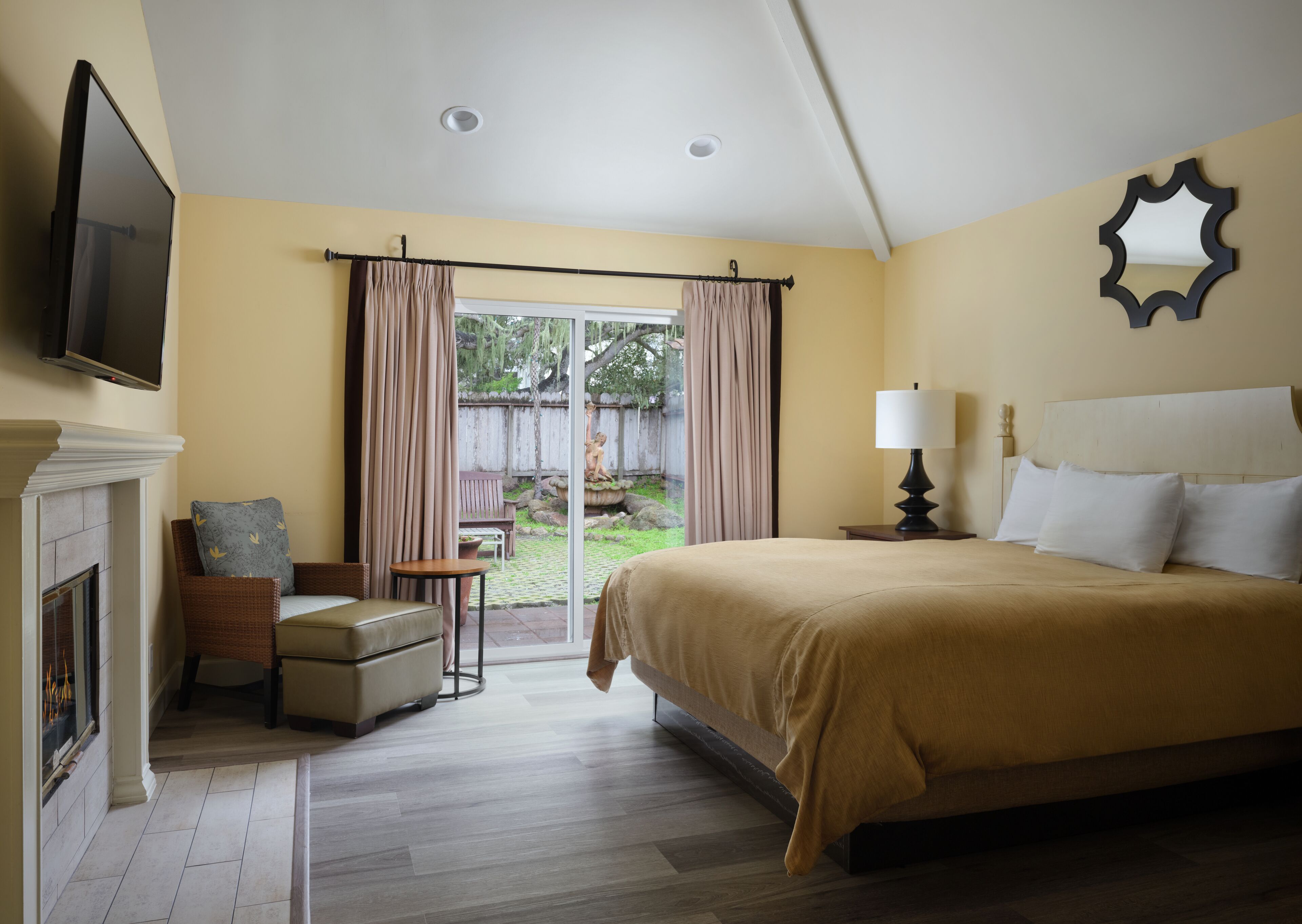 Habitación de hotel con una cama grande, televisor montado en la pared, chimenea y vistas al exterior.