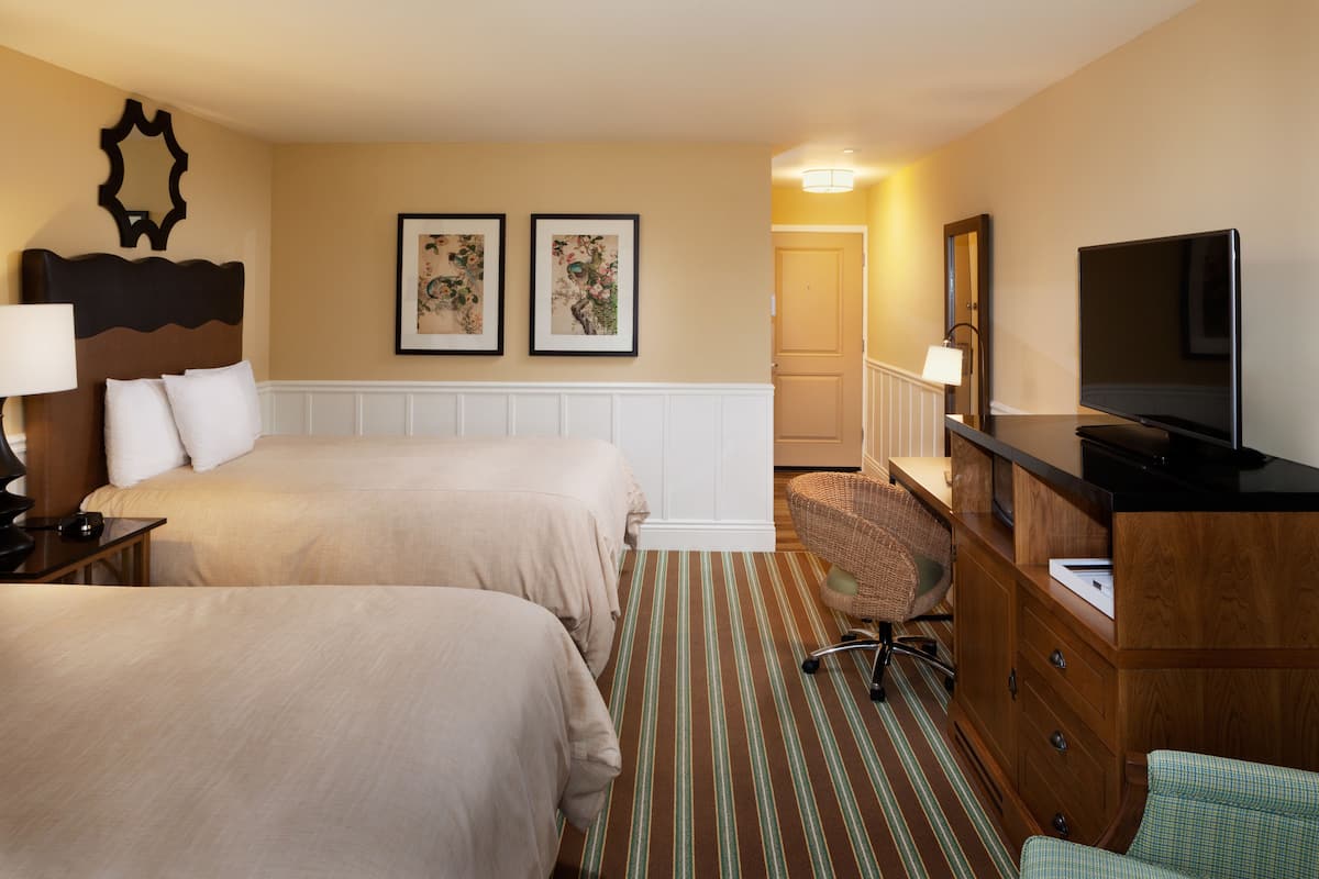 A hotel room with two beds, a television, a desk with a lamp, a chair, and a dresser.