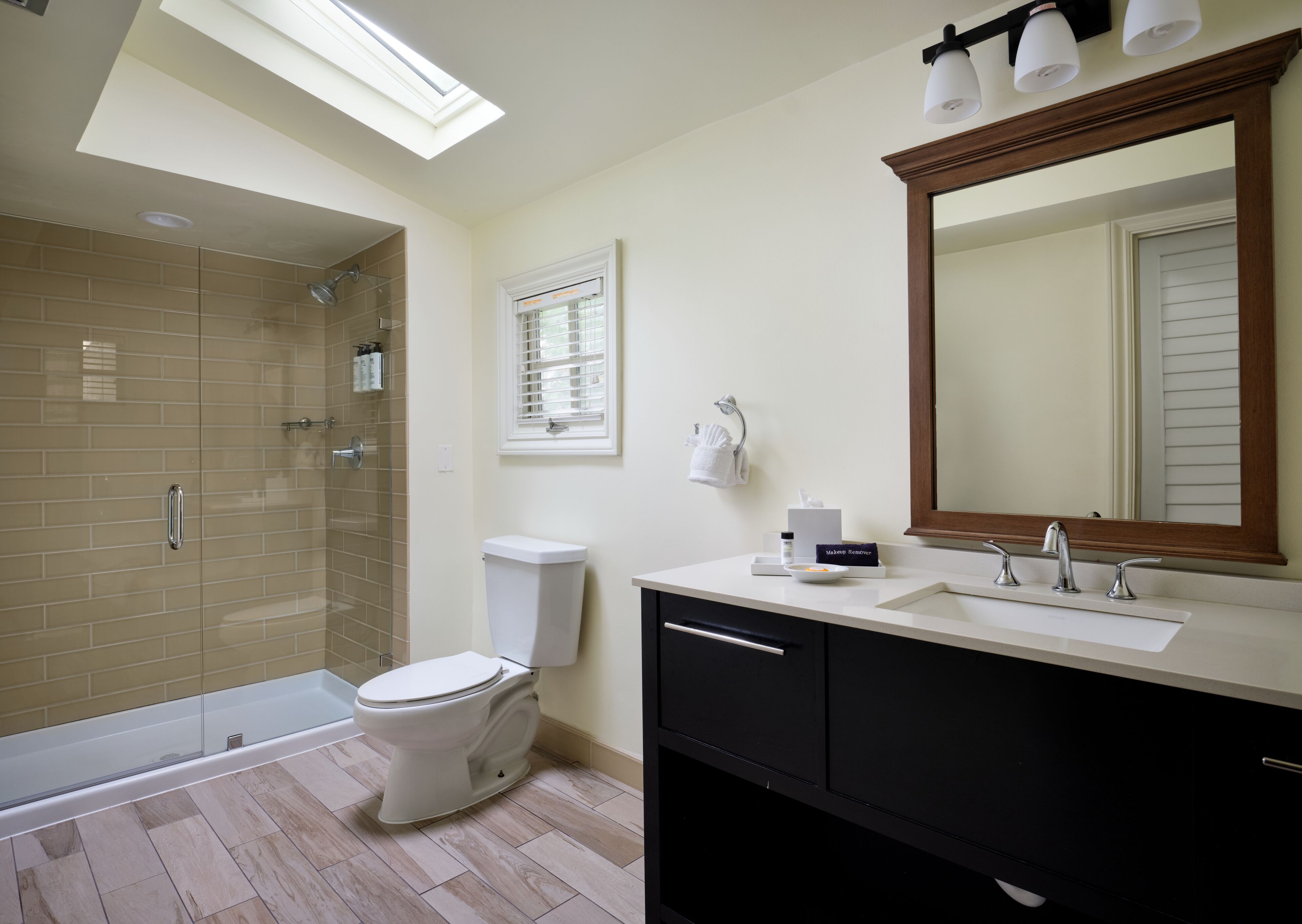 A modern bathroom with a glass-enclosed shower, a toilet, a vanity with a mirror, and a skylight.