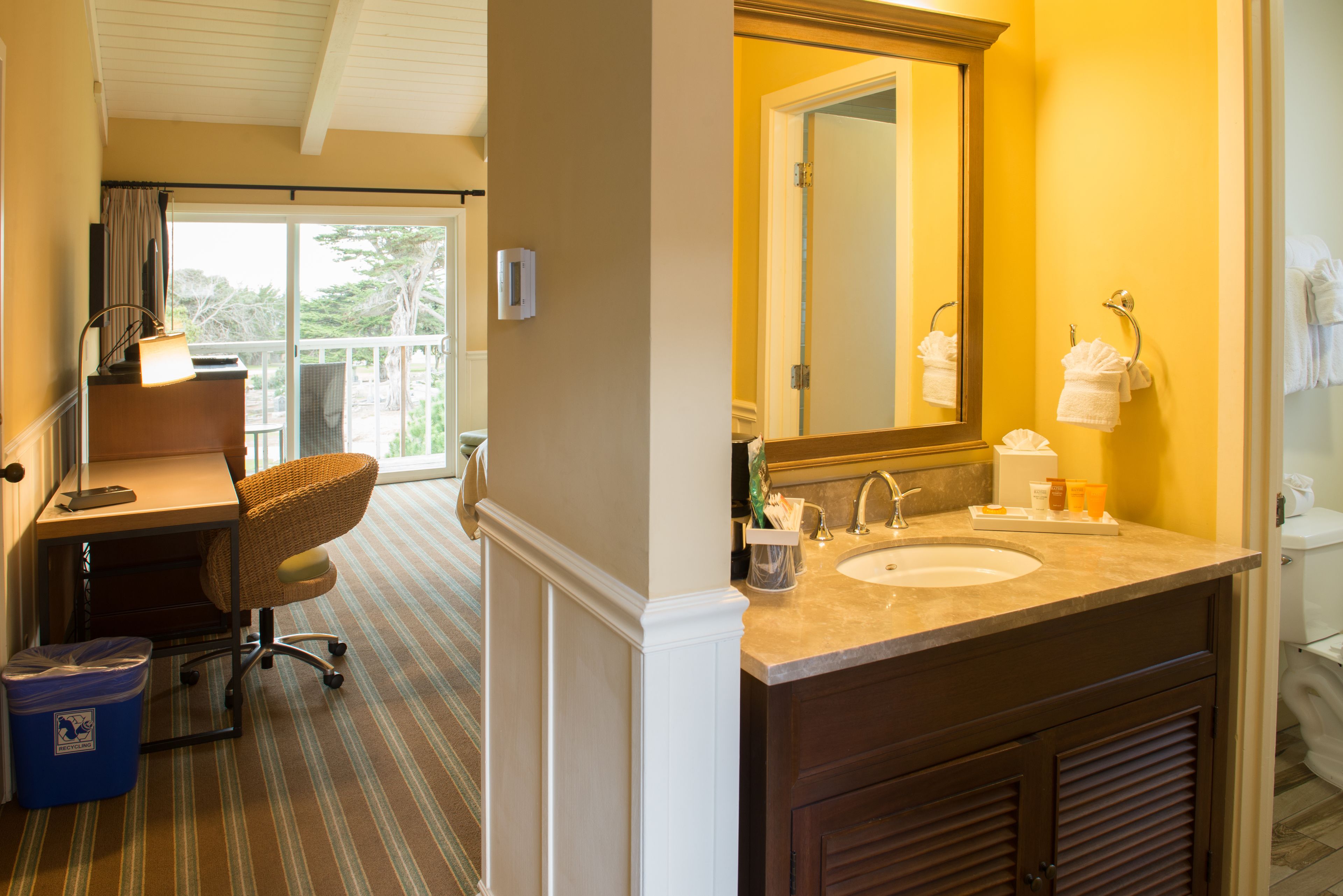 A hotel bathroom with a large mirror, two sinks, and a chair.