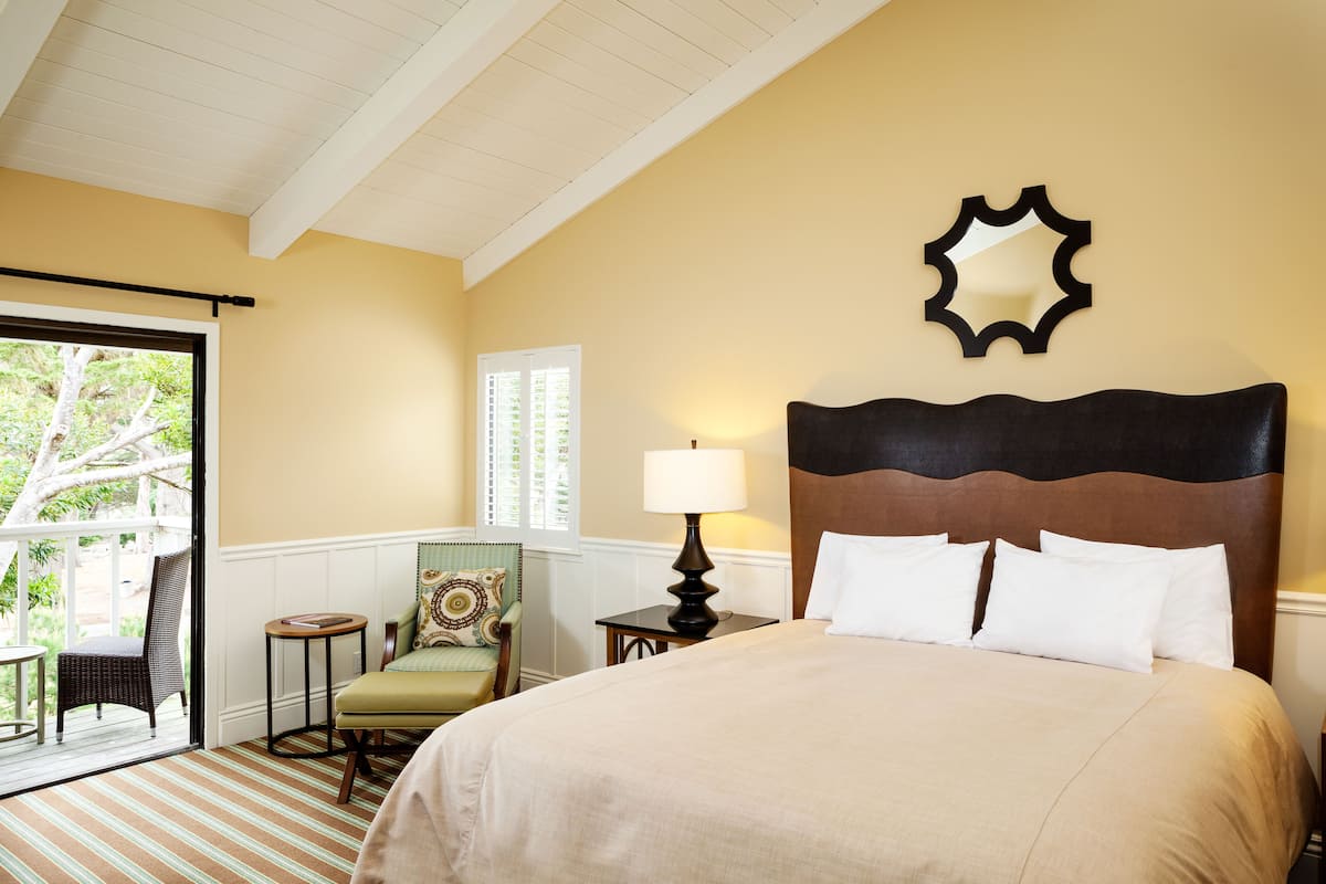A hotel room with a large bed, a nightstand with a lamp, a chair, and a window with blinds.