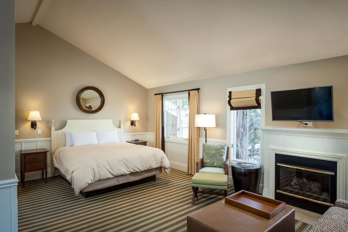 A hotel room with a large bed, a fireplace, a television, and a window with curtains.