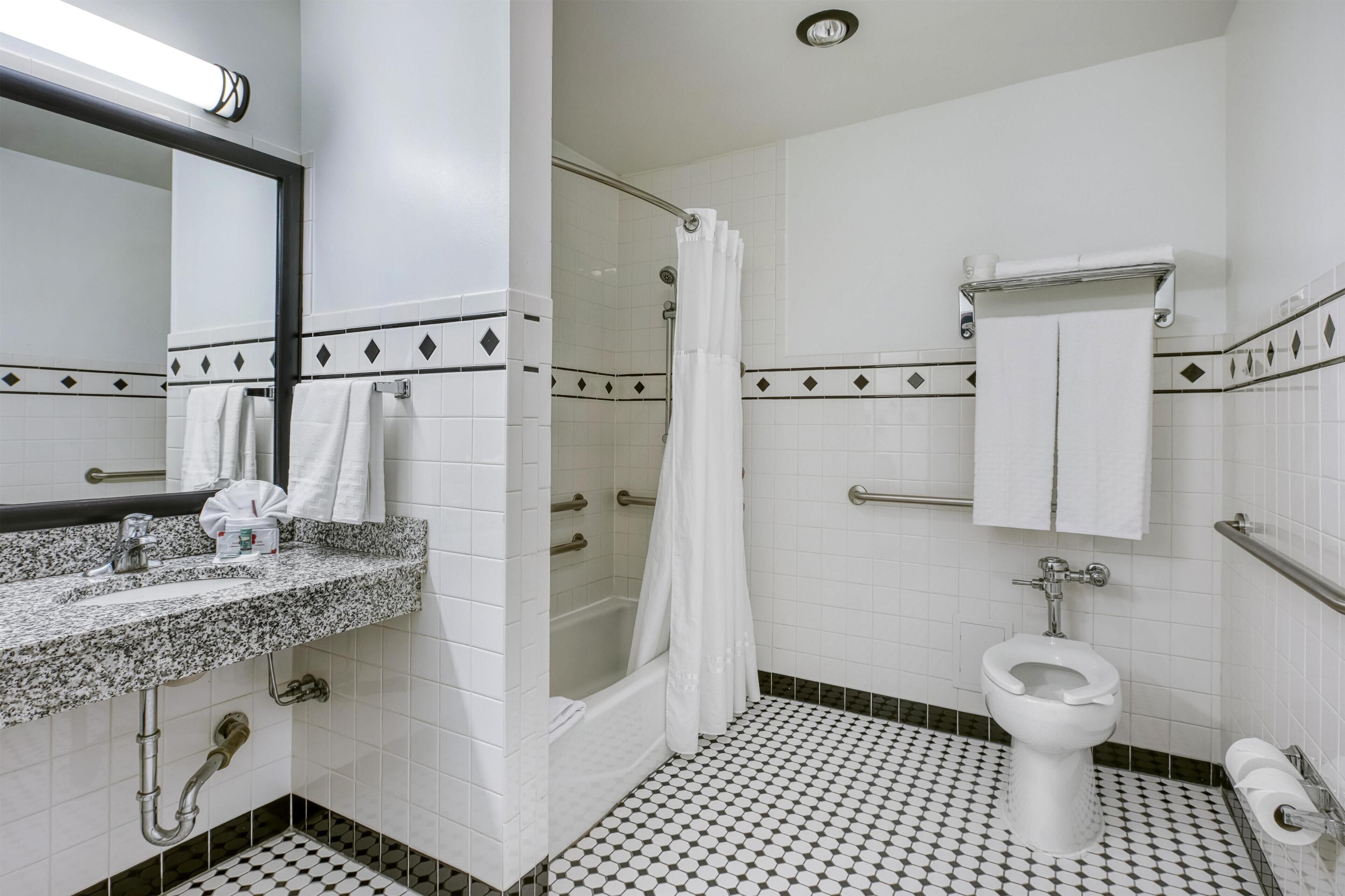 Un baño con lavamanos de granito, azulejos blancos, ducha e inodoro.