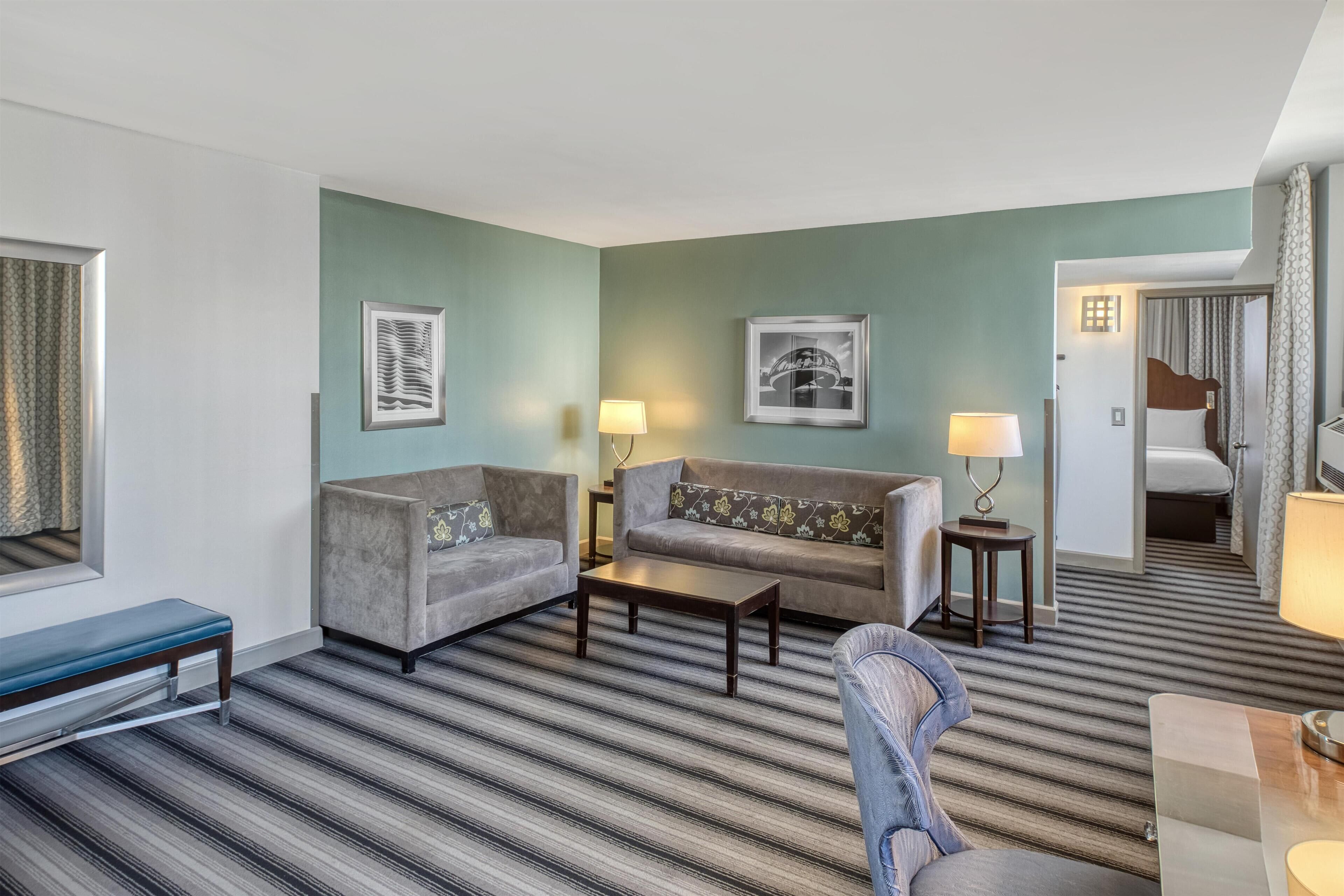 A hotel room with a striped carpet, two sofas, a coffee table, a bench, and a bed.
