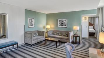 A hotel room with a striped carpet, two sofas, a coffee table, a bench, and a bed.