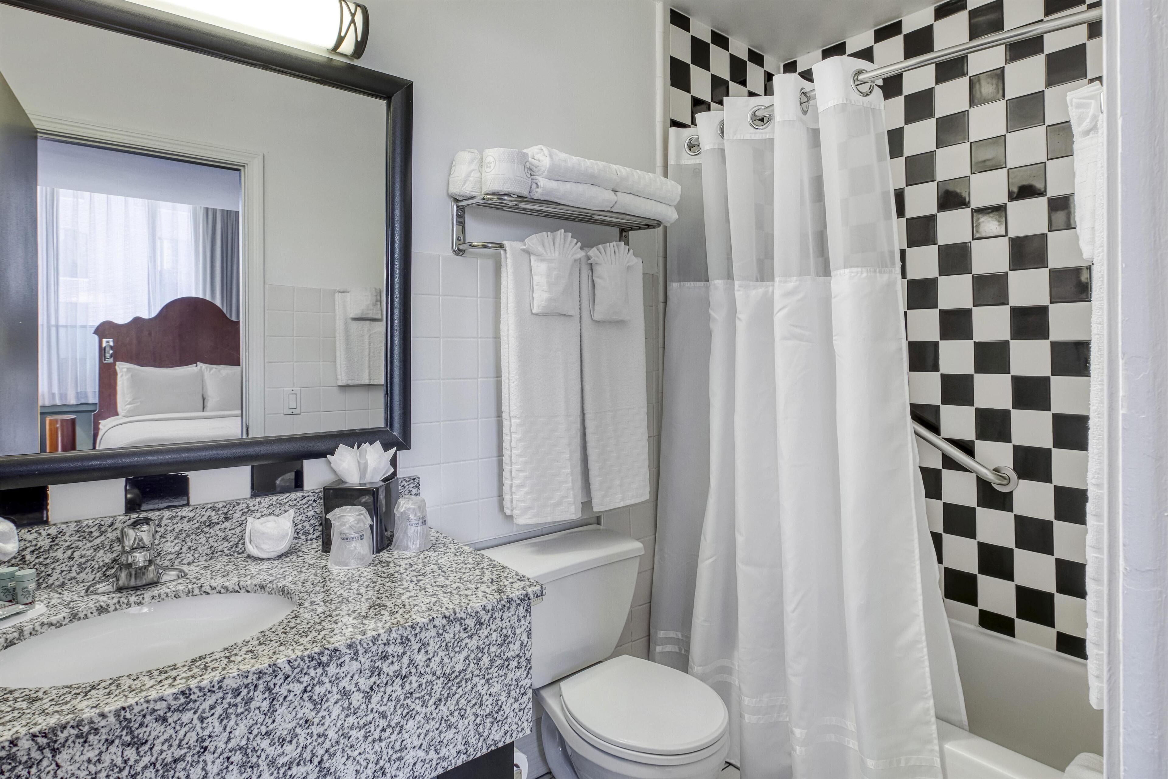 A bathroom with a granite countertop sink, a mirror, a toilet, and a shower with a checkered shower curtain.