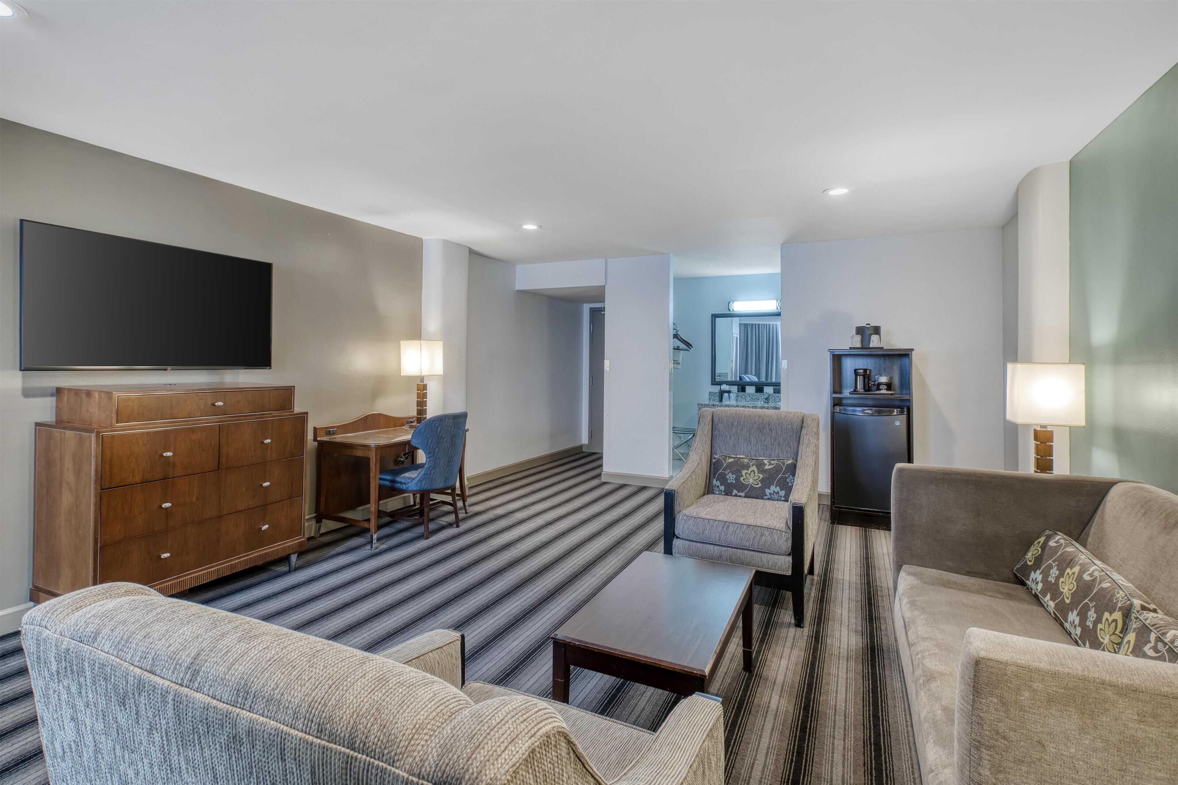 Une chambre d’hôtel équipée d’un téléviseur à écran plat, d’une commode en bois, d’un canapé, d’un fauteuil et d’une petite table.