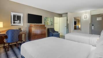 A hotel room with two beds, a desk with a chair, a dresser, a flat-screen TV, and artwork on the walls.