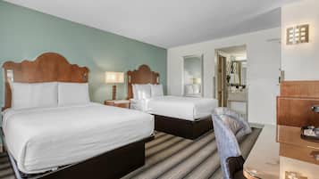 A hotel room with two beds, a desk, and a mirror.