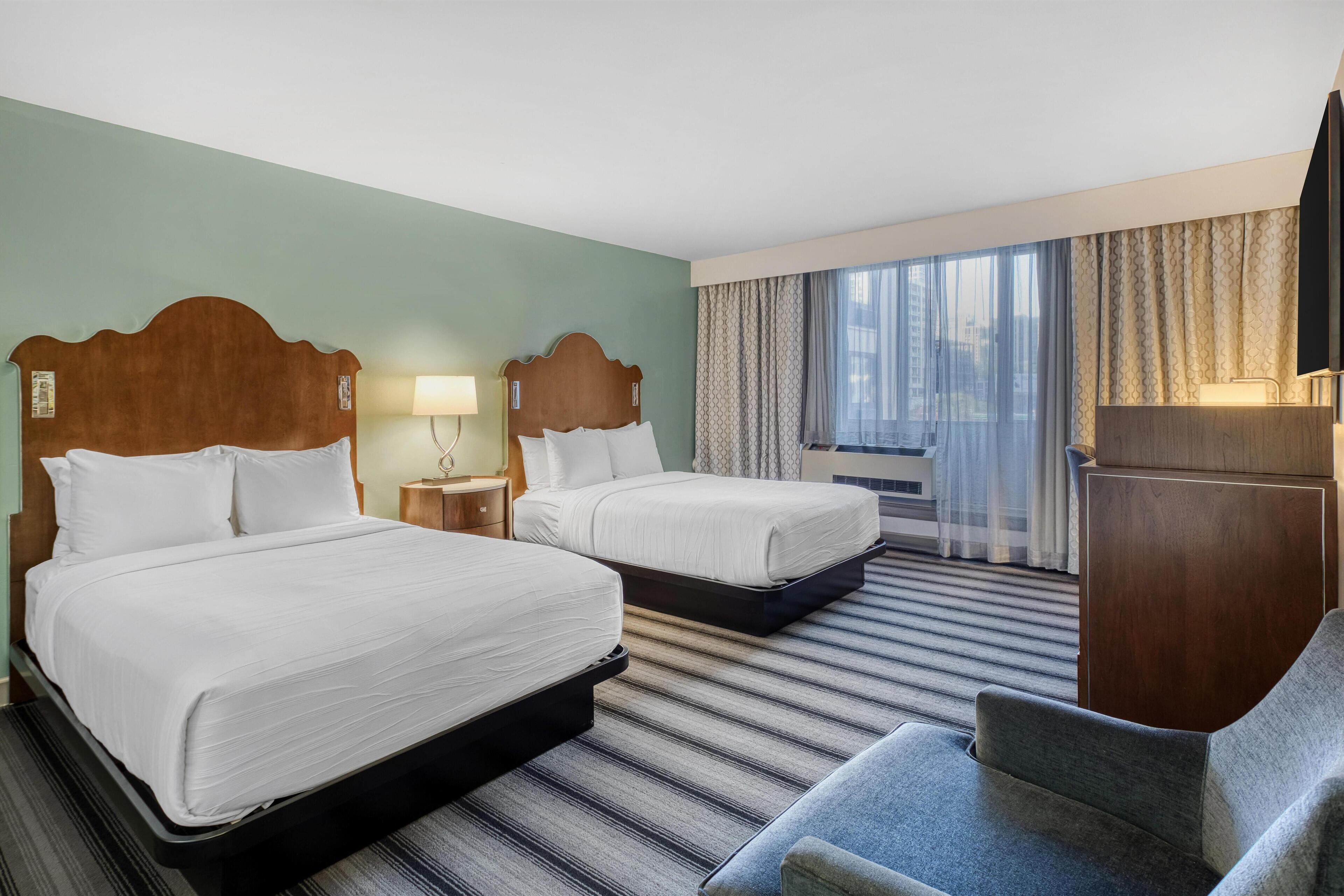 Une chambre d’hôtel avec deux lits, un bureau, une chaise, une télévision et une fenêtre avec des rideaux.