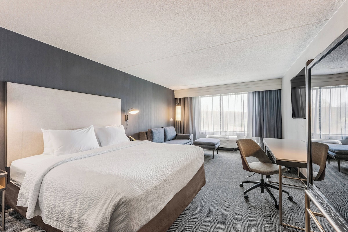 A hotel room with a large bed, a desk, a chair, a sofa, and a large mirror.
