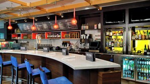 A bar area with a curved counter, blue bar stools, a menu board, and a refrigerated display of beverages. - Courtyard by Marriott Rockaway Mount Arlington (Mount Arlington)