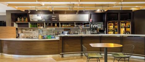 A modern bar area with a curved counter, two metal chairs, and a variety of bottles and glasses.