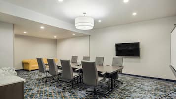 Una sala de conferencias con una gran mesa, sillas, un sofá y una pantalla de televisión.