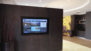 A digital display in a lobby with a dark wood panel backdrop, a large potted plant, and a colorful mural on the wall. - Courtyard by Marriott Rockaway Mount Arlington (Mount Arlington)