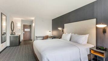 Een hotelkamer met een groot bed, nachtkastje, lamp en een bureau met stoel.