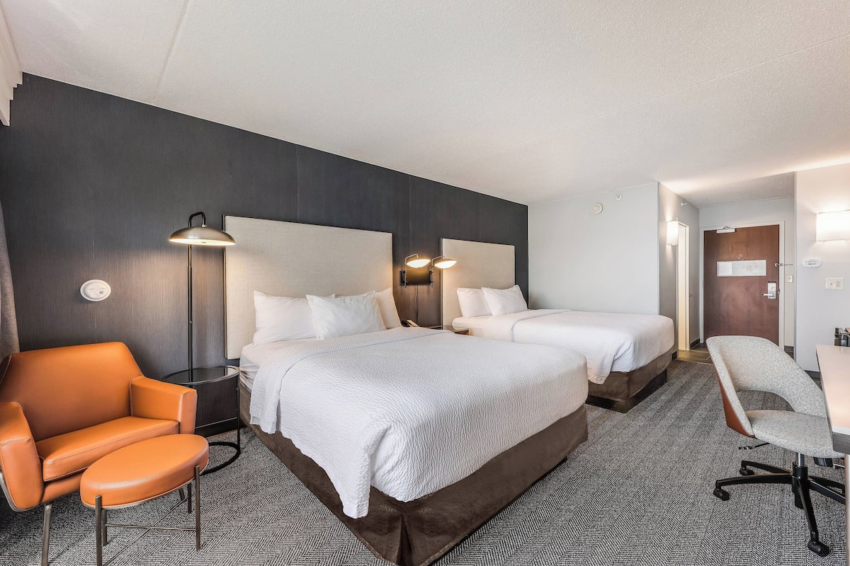 A hotel room with two beds, a sofa, a desk, and a chair.