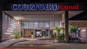 Eingang eines Courtyard Marriott Hotels mit moderner Fassade, Glasüren und Topfpflanzen.