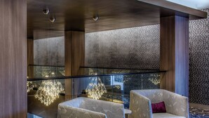 Ein moderner Lounge-Bereich mit gemusterten Sesseln, einer Glastrennwand und einem geometrischen Kronleuchter.