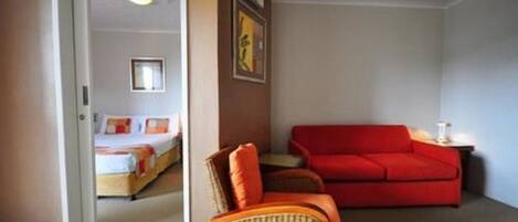 Una habitación con una cama, un sofá rojo y una silla de mimbre.