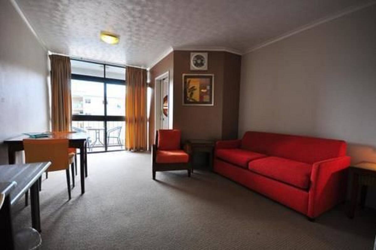A hotel room with a red sofa, a small table, a chair, and a view through a large window.