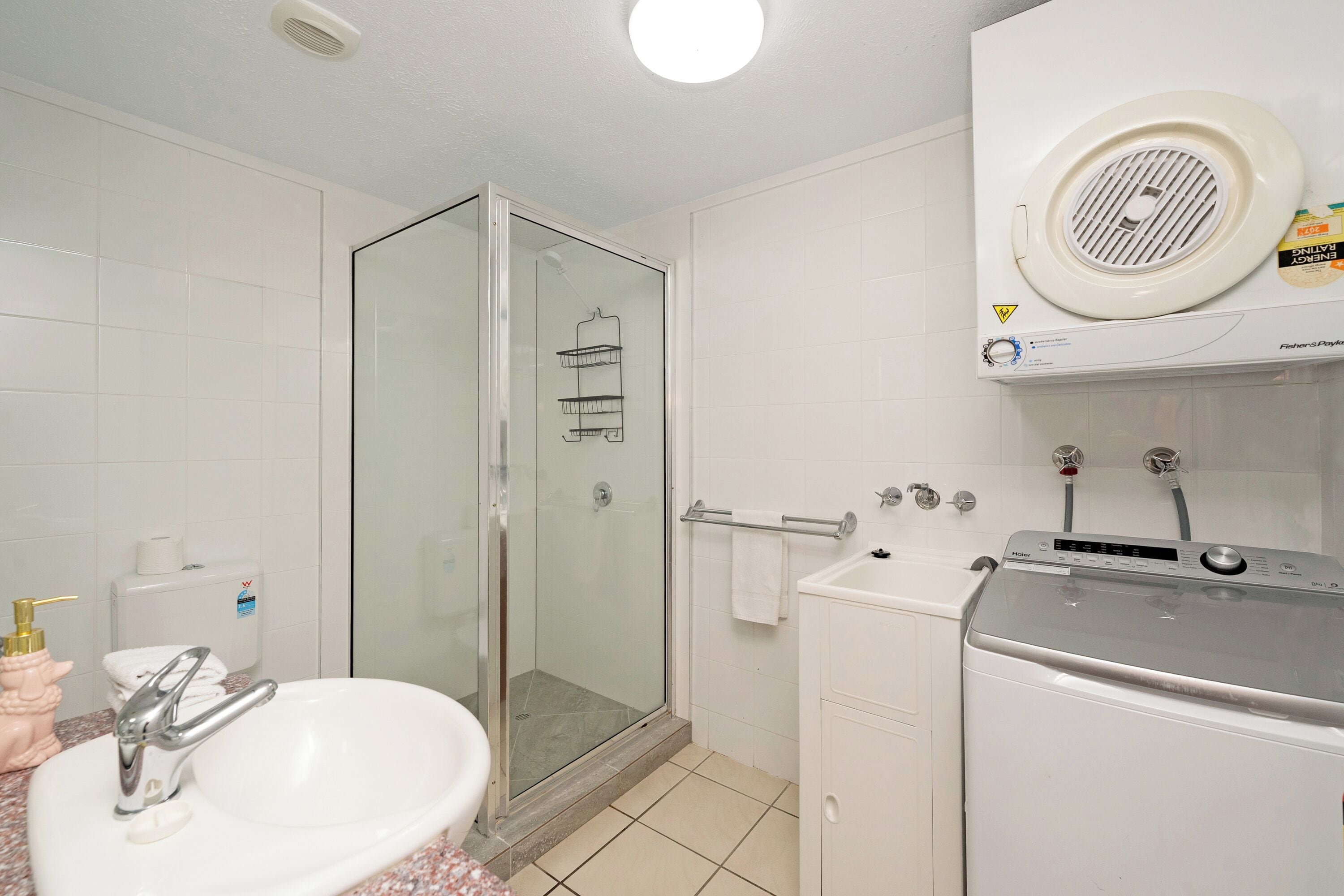 A bathroom with a glass shower enclosure, a sink with a faucet, a toilet, and a washing machine.