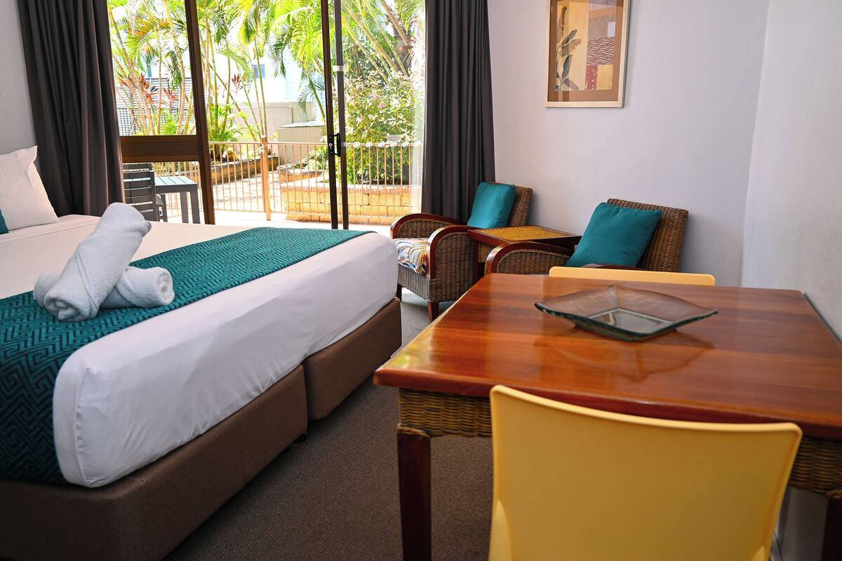 A hotel room with a bed, a dining table, and a view of the outdoors.