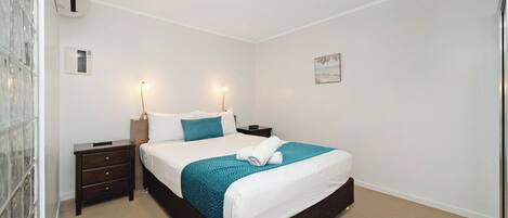 A neatly arranged bedroom with a bed, bedside tables, a nightstand, a wall-mounted air conditioner, and a ceiling light.