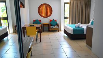 A hotel room with a bed, a desk, two chairs, a round wall decoration, and a view of the outdoors.