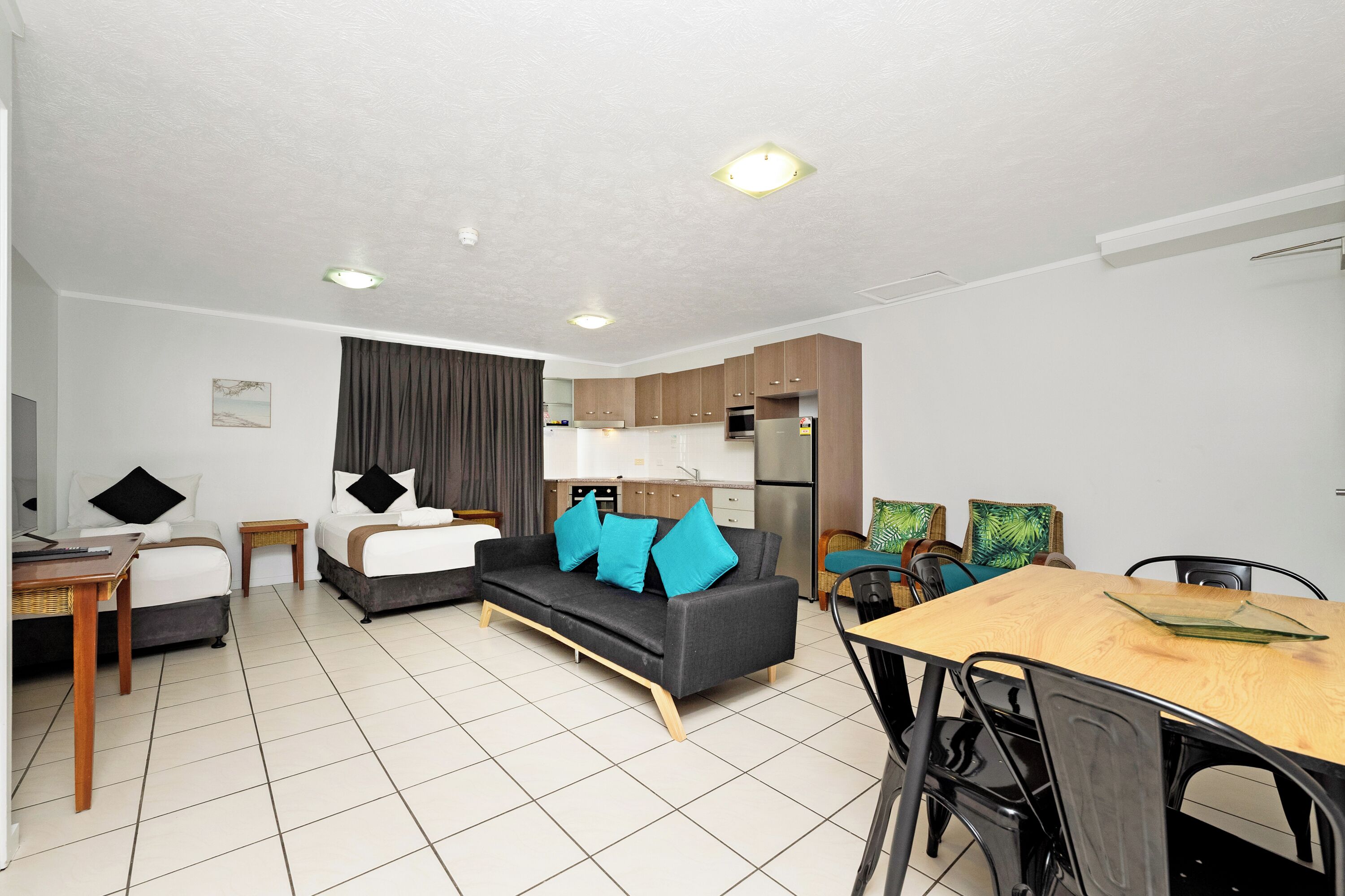 A modern hotel room with a sofa, a dining table, a kitchen area, and a separate sleeping area.