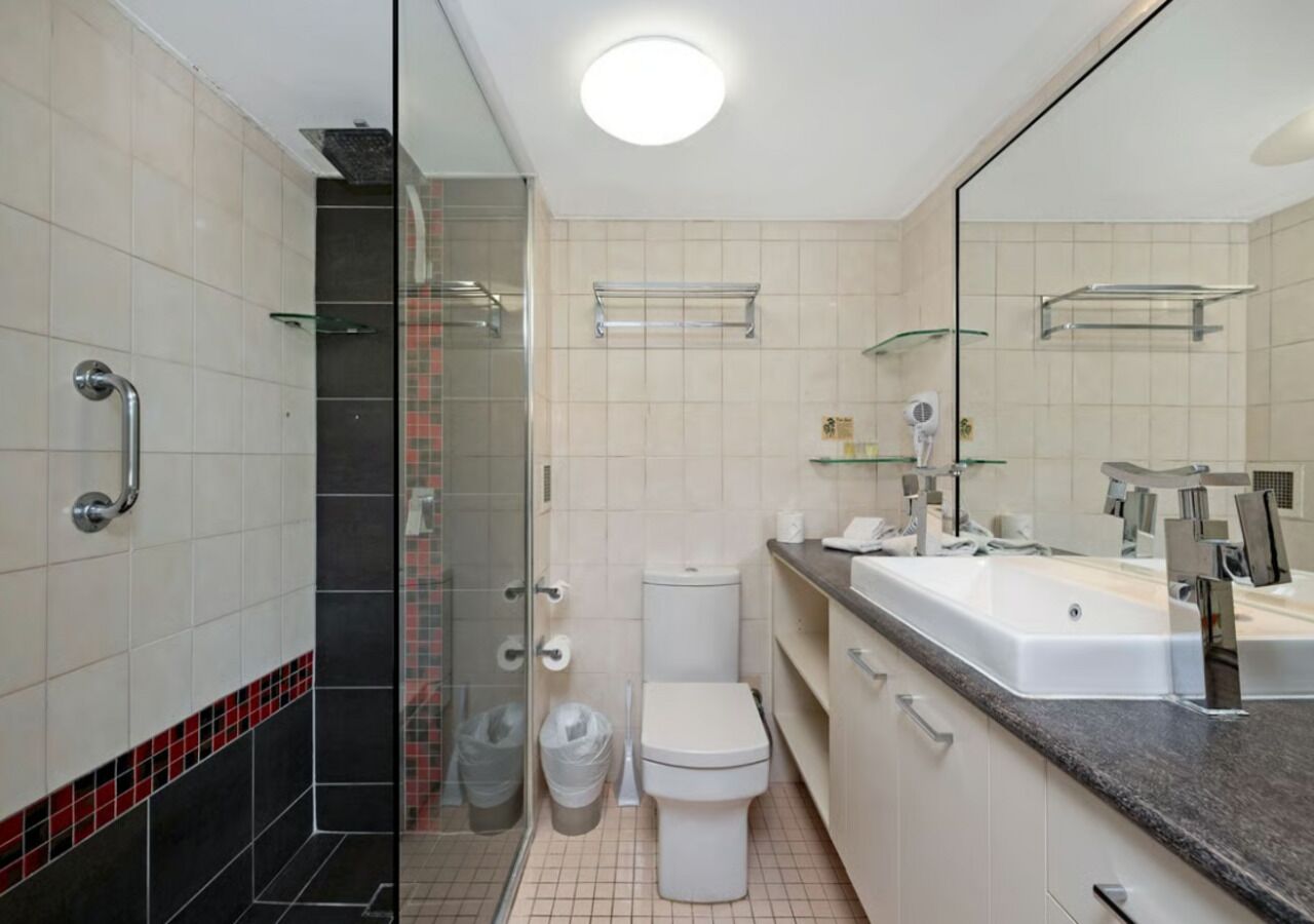 Une salle de bain moderne avec une douche à parois de verre, des toilettes blanches, un grand lavabo avec un miroir et des murs carrelés.