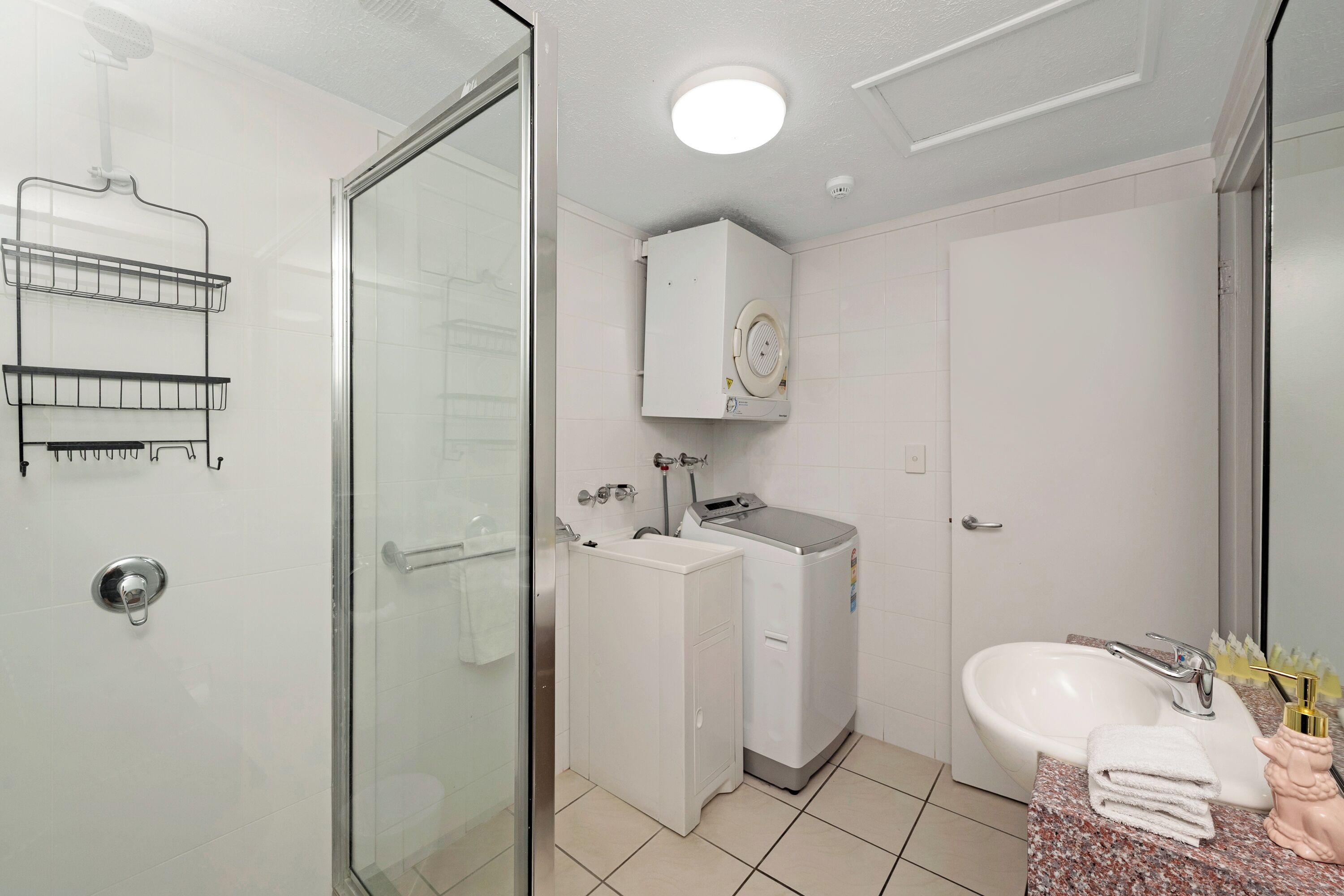 A bathroom with a glass shower enclosure, a white sink, a washing machine, and a cabinet above the sink.