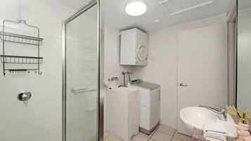 Een badkamer met een glazen douchecabine, een wit wastafelmeubel, een wasmachine en een kastje boven de wastafel.