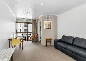 Una sala de estar moderna con un sofá negro, una mesa de comedor con sillas amarillas y una vista a través de una puerta de cristal.
