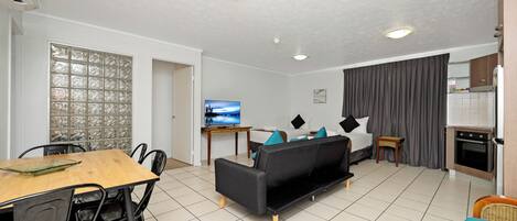 Ein Wohnzimmer mit Sofa, Esstisch, Stühlen, einem Fernseher und einer Küchenzeile mit Herd.
