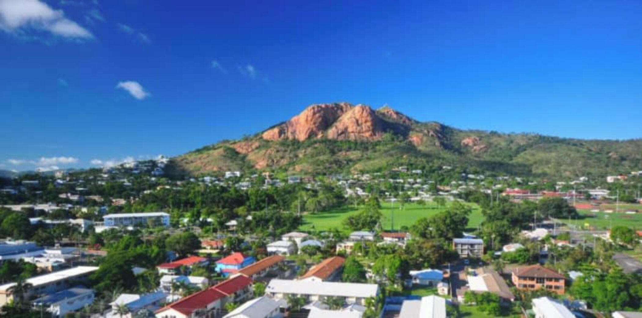 A town with a prominent mountain in the background, houses with red roofs, and green spaces.