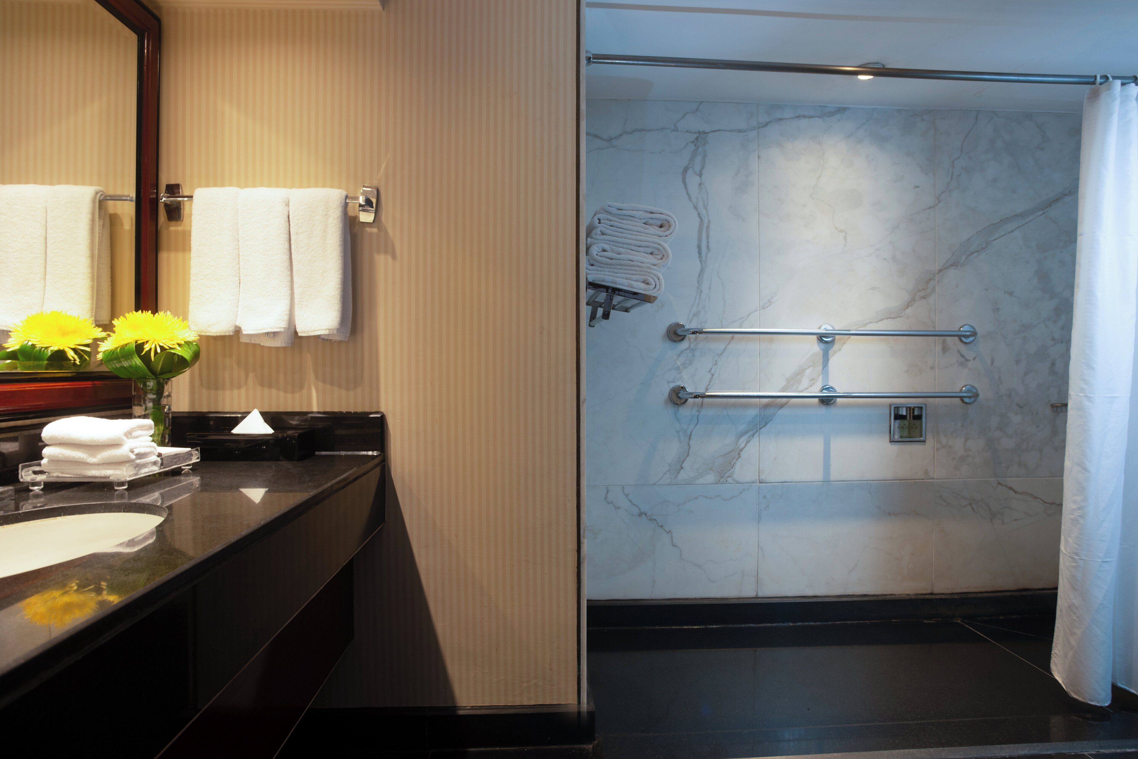 A bathroom with a marble shower wall, a glass-enclosed shower, and a vanity with a mirror and towel rack.