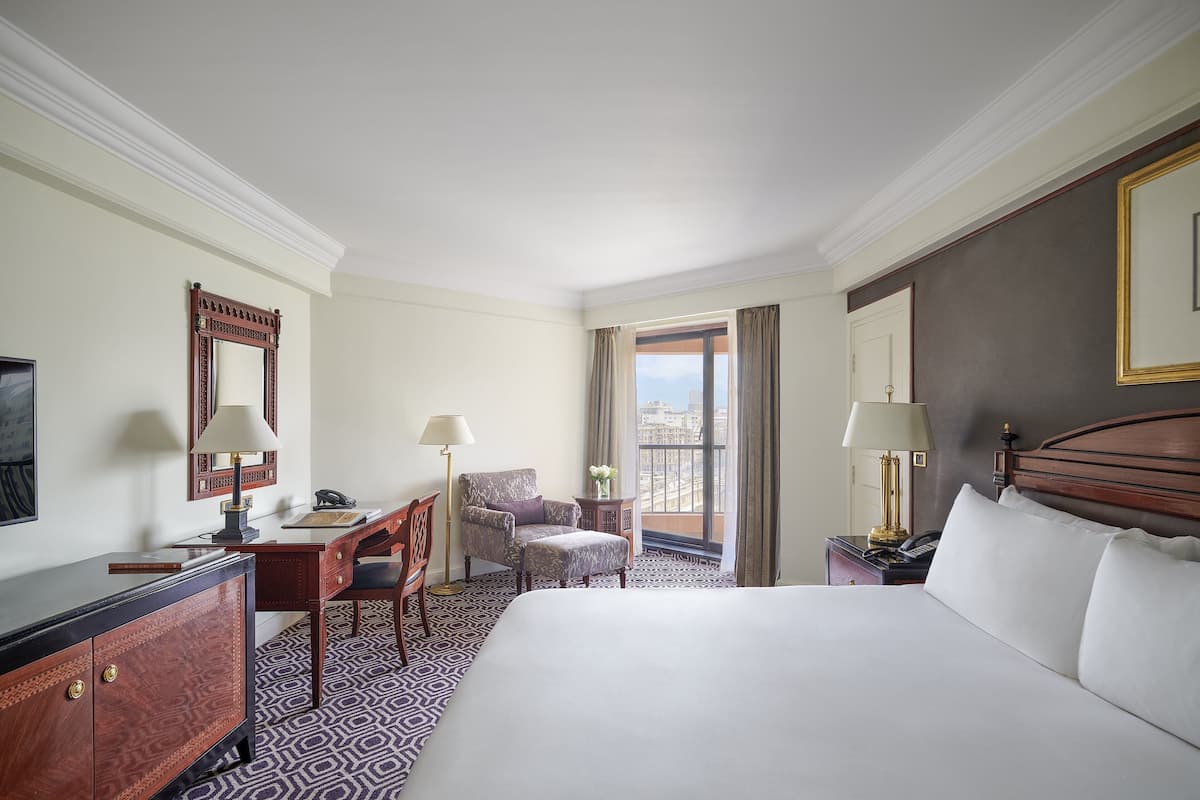 A hotel room with a large bed, a desk, a chair, a dresser, and a balcony with a view.